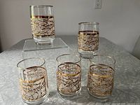 Group of five vintage Dominion Glass Crackle Ice glasses with gold accents arranged on a reflective surface showing all glasses.