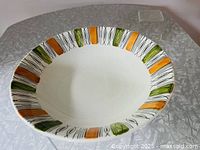 Top angled view of a round ceramic bowl with geometric pattern in dark green, orange, and black on white background.