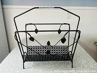 Front view of vintage black metal magazine rack showing leaf design and woven vinyl handle