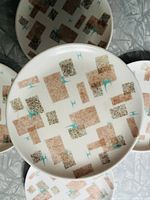Set of five round Melmac plates with tan, brown, and turquoise graphic pattern, laid out on a surface.