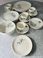 Photo showing all dish pieces including cups and saucers with bamboo leaf designs in green and brown on white.