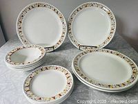 Full set of vintage Steelite Fanfare pattern dishware from the 1950s, showing arrangement of dinner plates, side plates, and bowls with colorful graphic rim pattern.