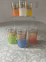 Full set of six vintage sugar frosted glasses in various colors arranged on clear display stand, showing gold band detailing and color vibrance.