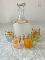 Full view of the vintage sugar frosted glasses in various colors and the glass decanter with gold bands.