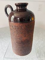 Front view of tall pottery vase, showing textured lower body and smooth glazed upper section with handle
