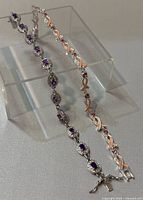 Two bracelets displayed on a clear acrylic stand showing the purple rhinestone bracelet and the pink breast cancer awareness ribbon bracelet