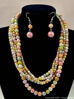 Close-up view of the multi-strand beaded necklace and matching earrings displayed on a black bust. Beads are glossy and come in multiple colors such as pink, green, gold, and orange.