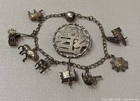 Antique Chinese silver charm bracelet with 8 distinct charms laid flat for full view.