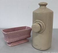Beige Govancroft pottery foot warmer and pink McCoy pottery footed planter side by side on a neutral background