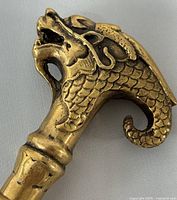 Close-up of the dragon head handle of the brass walking stick showing detailed scales and facial features