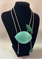 Front view of the modernist green acrylic necklace displayed on a black mannequin stand showing the large leaf-shaped pendant, smaller oval acrylic piece, and heart-shaped ends on the adjustable cord.