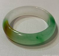 Natural jade bangle, D shaped, showing green and brown hues with smooth surface and minor wear.