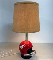 Desk lamp with beige fabric lampshade and red football helmet base showing Mustang logo