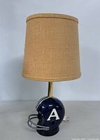 Full view of desk lamp with football helmet base and beige fabric lampshade.