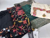Four shawls folded together showing varied floral embroidery and border styles.