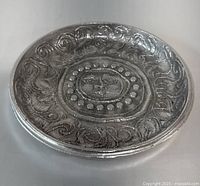 Side angle view of the circular aluminum wall hanging platter showing depth and raised sun face design