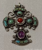 Front view of vintage Mexican 925 silver cross pendant with turquoise, coral, and amethyst stones on a flat surface.