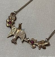 Close-up of the swallow pendant with floral decorations and red gemstones to show design details and minor wear.