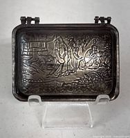 Top view of engraved metal case showing intricate design of figures and landscape.