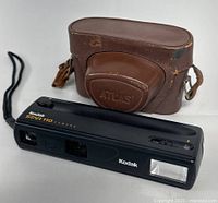 Photo of Kodak Star 110 camera next to brown leather Atlas case showing minor wear