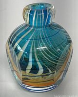 Front and slightly angled view of blue hand blown glass vase or perfume bottle with white and orange swirl patterns, showing thick clear glass and rounded body.
