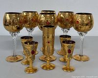 Front view of all 8 glasses showing gold and red jewel decoration with twisted clear stems on goblets.
