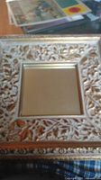 Close-up photo of one square mirror showing its ornate carved floral frame finished in gold.