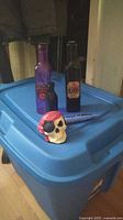 Blue storage bin with Halloween items on top: skull figure, two decorative bottles, blue plastic knife.