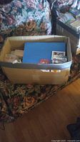A large cardboard box containing football cards, some in plastic sleeves and organized in a blue binder, placed on a floral patterned couch.