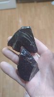 Two dark glassy obsidian rocks held in hand with visible conchoidal fractures