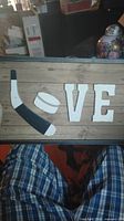 Photo of a decorative wooden wall art with the word LOVE where the L is formed by a hockey stick and a puck on a wooden plank background.