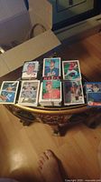 Photo showing sixteen vintage baseball cards in two groups on a wooden table, depicting various players and teams.