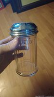 Handheld photo of a clear ribbed glass sugar shaker with a shiny silver metal screw-on lid.