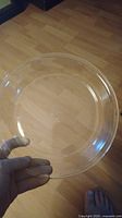 Photo showing person holding the clear 9 inch glass pie pan, showcasing the item and size against a wooden floor background.