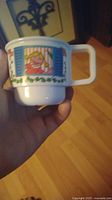 White ceramic cup held in hand showing Sesame Street character in window and surrounding colorful design