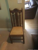 Front view of an antique wooden chair with a carved backrest and cushioned seat in brown tones in a residential room setting.