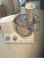 Photo shows Braun CombiMax 600 food processor on countertop with dual control knobs, clear plastic bowl with handle, and attached feeder chute for processing.