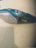 Side view of Dirt Devil Quick Flip handheld vacuum, blue and gray body with clear dust container showing branding and model details.