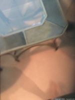 Photo showing the corner and underside of the glass and metal square table with bronze frame and curved metal supports.