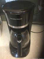 Photo of the Hamilton Beach black drip coffee maker showing front side with glass carafe on heating plate