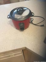 Red Salton rice cooker on countertop with lid and power cord visible