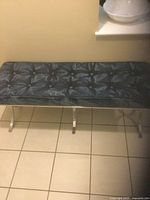 Blue button-tufted fabric upholstered bench with polished metal legs on tiled floor