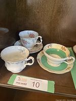 Lot of three china teacups; two with saucers, one without. Displayed on wood shelf with auction card.
