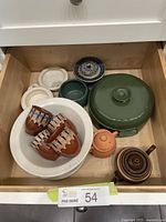 Full view of all ceramic pieces in drawer, showing various mugs, bowls, covered dish, and teapots arranged neatly.