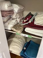 Shelf with assorted folded linens including pillowcases, sheet sets, mattress covers, chenille bedspread, a small blue blanket, hot water bottle and heat pad pouch.