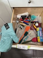 Drawer with colorful kitchen utensils, including spatulas, ladle, slotted spoon, tongs, bottle brush, toothpicks, straws, and oven mitts.