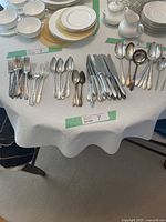 Full layout of community plate silverware including forks, knives, spoons, serving utensils, and plates in the background.