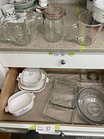 Four cornflower blue CorningWare baking dishes with white interiors, various glass Pyrex baking pans, and glass jar with sealer in kitchen drawer