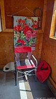 Full view of red collapsible outdoor deluxe chair with attached side table and hanging floral tapestry on wall.