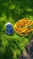 Garden hose coiled on grass next to electronic garden fountain unit.